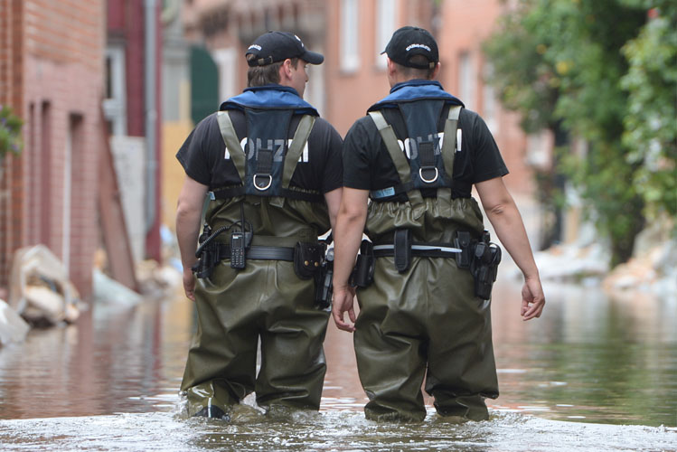 Zwei Polizisten laufen durch das Hochwasser in einer Stadt mit Schutzkleidung