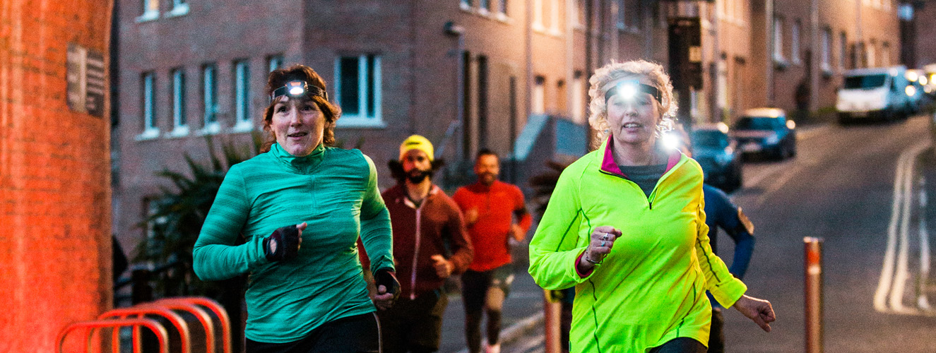 Menschen joggen in der Dämmerung mit Stirnlampe auf dem Kopf und fügen sich damit dem Zeitalter der Fitness