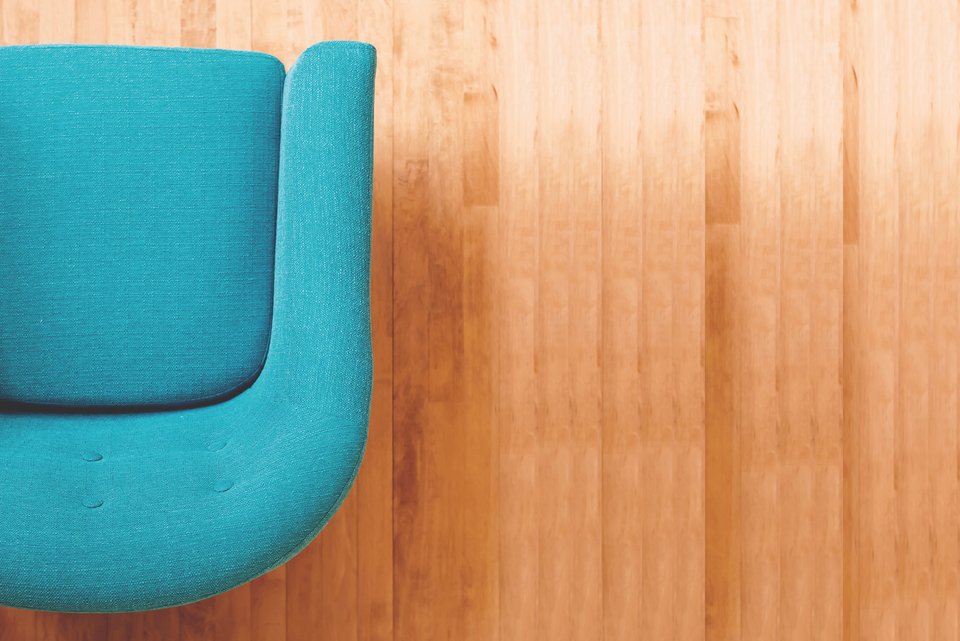 Ein blauer Sessel steht in einem hellen Raum mit hellem Holzboden, in dem eine Psychotherapie stattfindet.