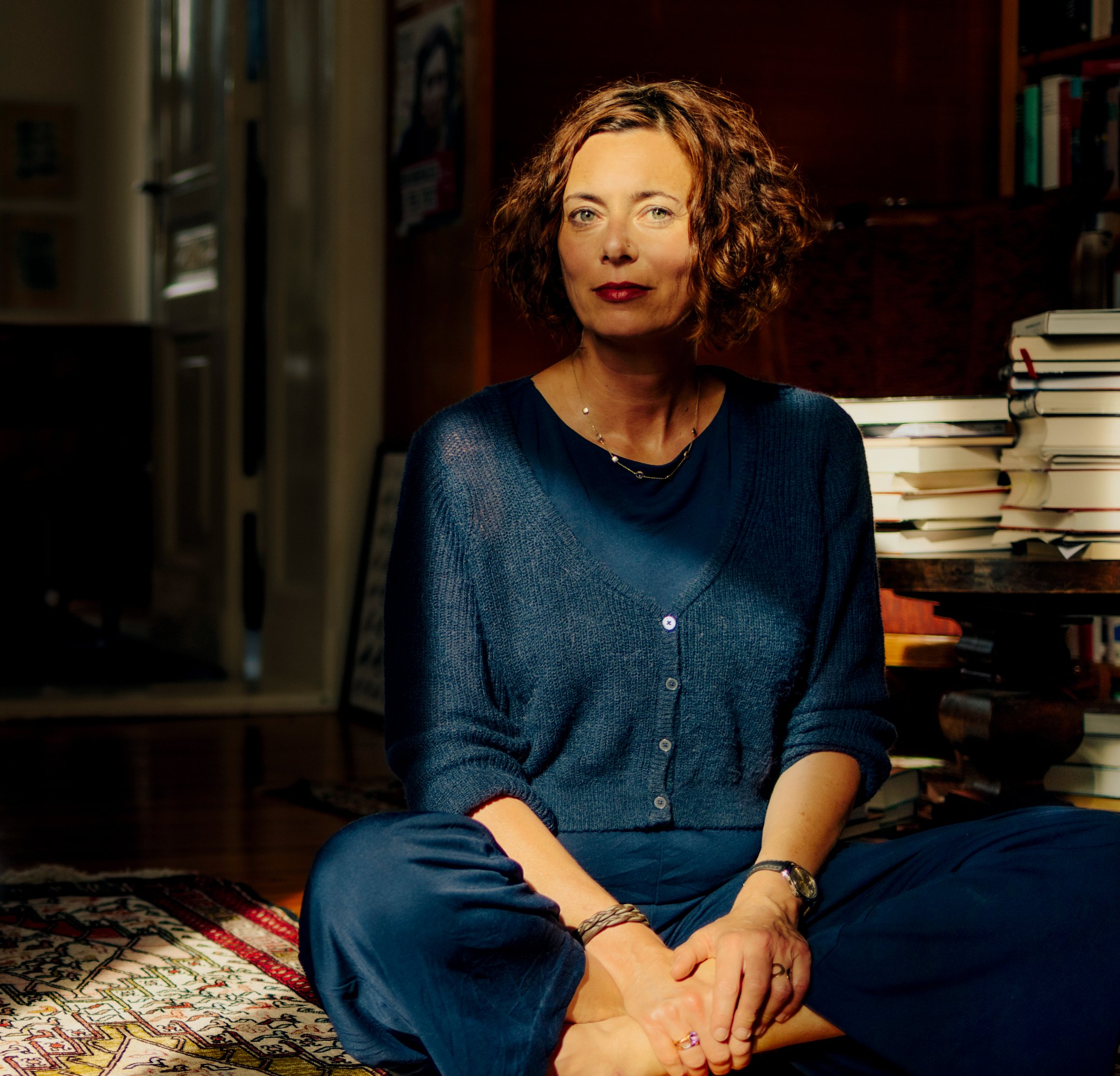 Das Foto zeigt die Autorin Eva Menasse, wie sie im Schneidersitz in Ihrem Wohnzimmer auf dem Boden sitzt.