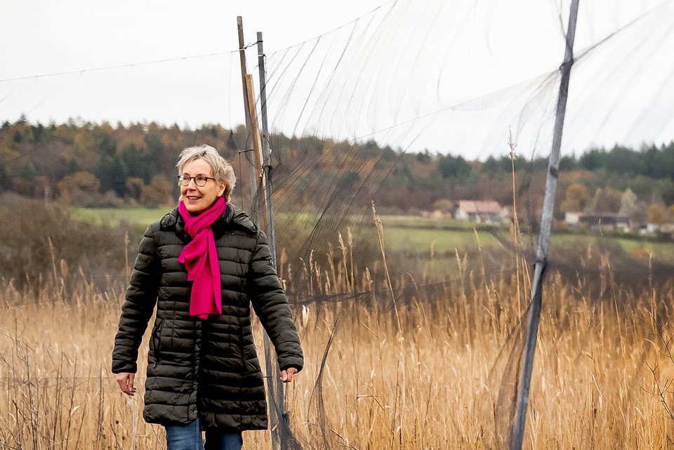 Die Autorin Ilona Jerger läuft in der Natur an einem Netz vorbei
