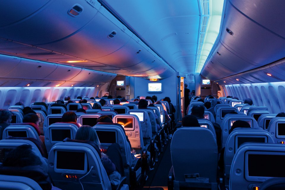 In einer Flugzeugkabine sind viele Sitzplätze mit Passagieren zu sehen