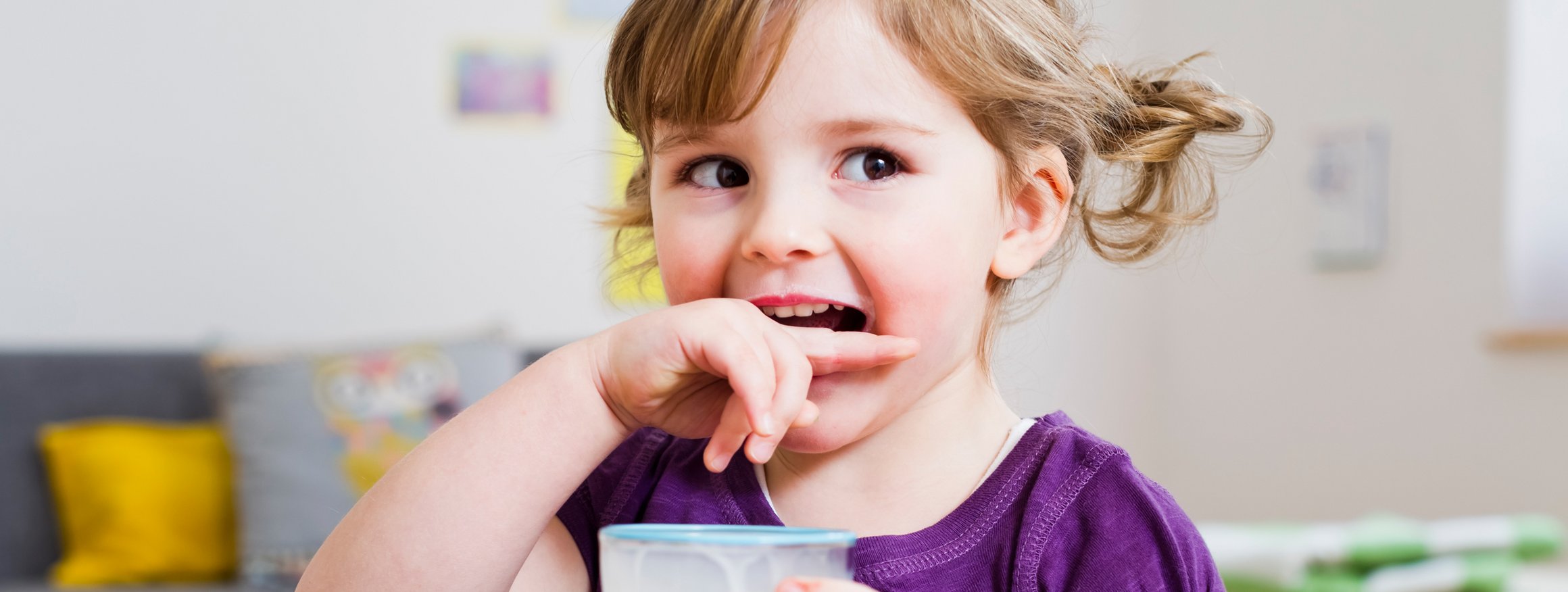 Ein kleines Mädchen hält ein Glas Milch in der Hand und lächelt verschmitzt