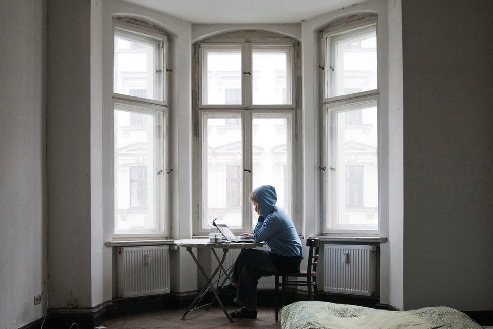 Eine Frau sitzt einsam in einer Stadtwohnung an ihrem Laptop am Fenster in einem Erker
