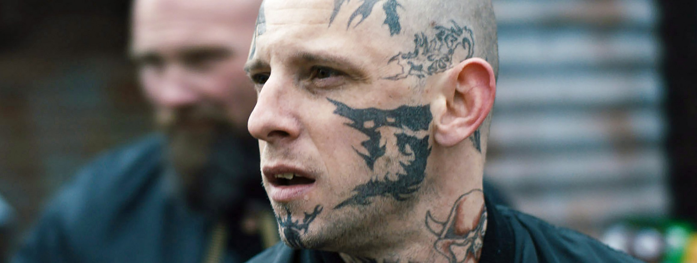 Ein Skinhead mit Tattoos im Gesicht schaut aggressiv