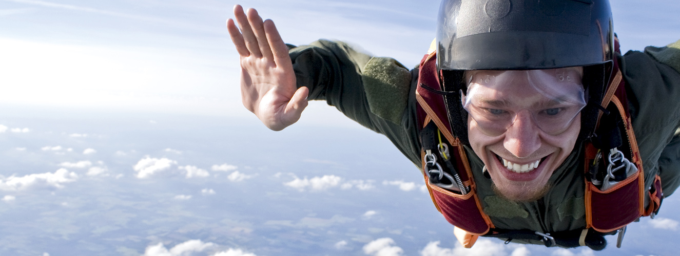 Das Bild zeigt einen lächelnden Basejumper über den Wolken als Beispiel für Extremsport in der Natur