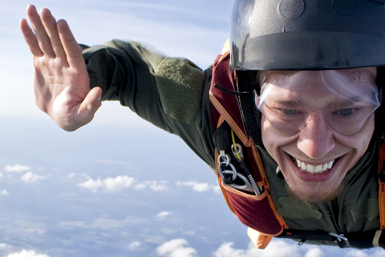Das Bild zeigt einen lächelnden Basejumper über den Wolken als Beispiel für Extremsport in der Natur