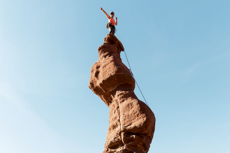 Eine Frau auf dem Gipfel eines spitzen Felsens in Moab, USA, freut sich über den Ausblick.