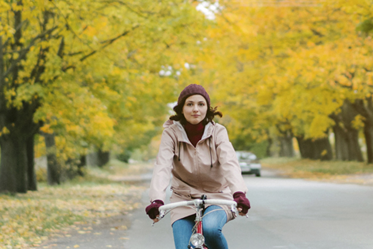 Eine Frau fährt Fahrrad auf einer herbstlichen Allee und nähert sich so der Natur an