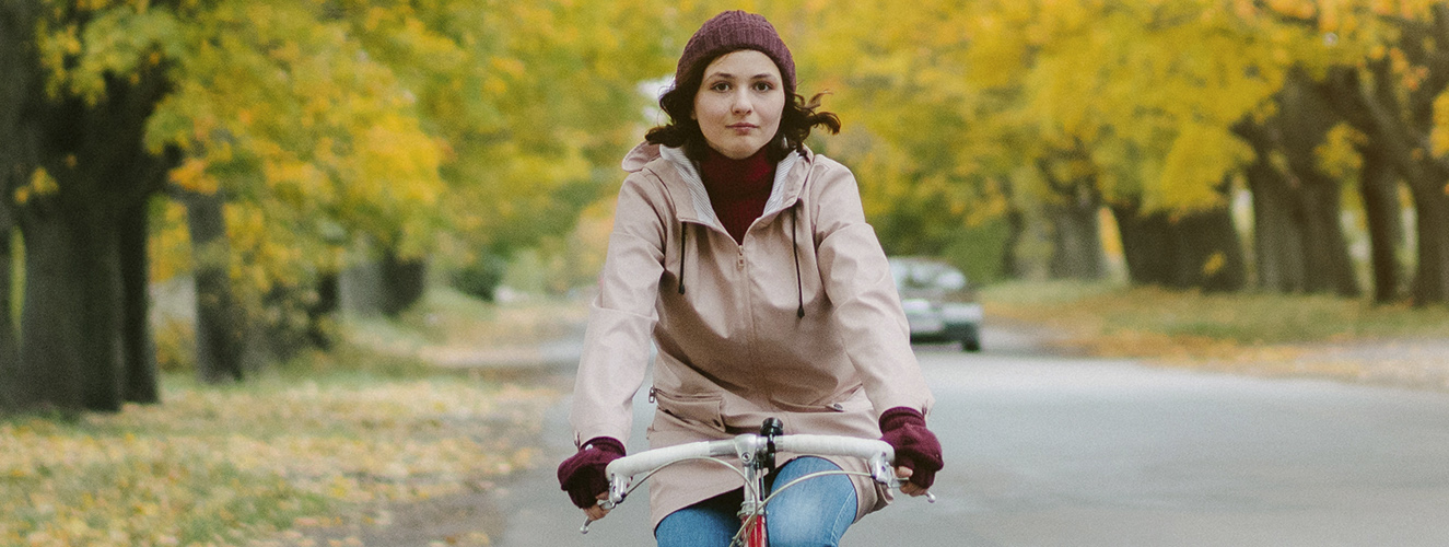 Eine Frau fährt Fahrrad auf einer herbstlichen Allee und nähert sich so der Natur an