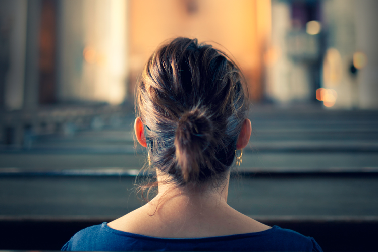 Foto zeigt eine Frau, die auf einer Kirchenbank in einer großen Kirche sitzt