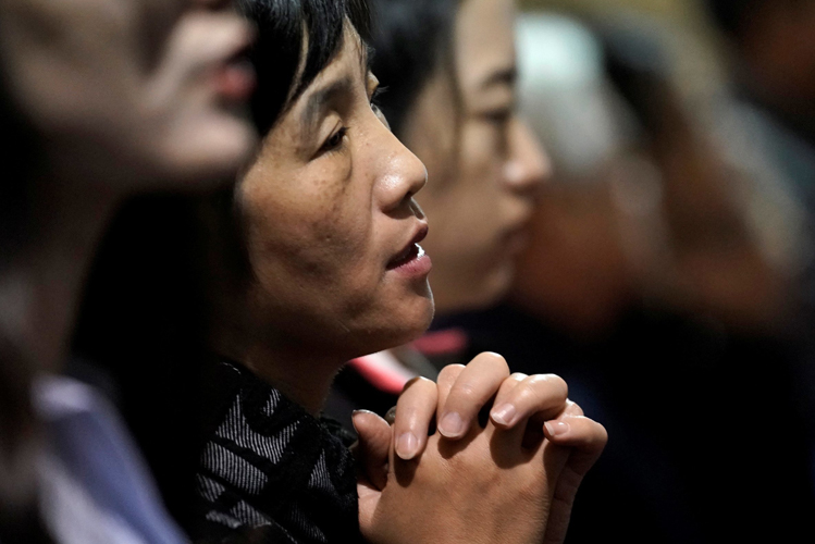 Eine Frau sitzt in einer vollen Kirchenbank mit gefalteten Händen und betet andächtig