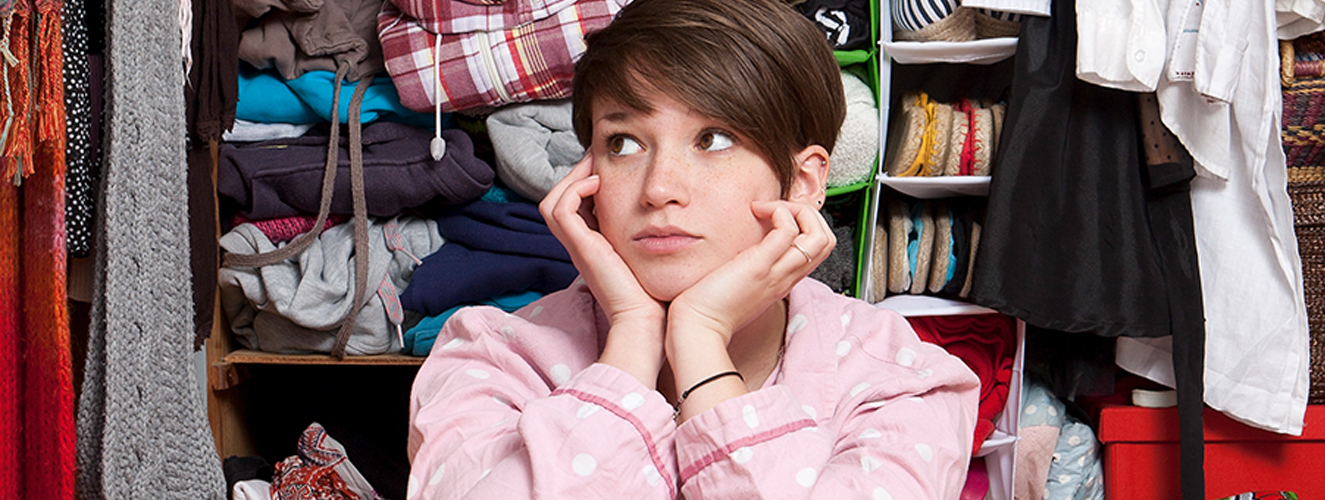 Das Foto zeigt eine junge Frau, die vor ihrem Kleiderschrank sitzt.