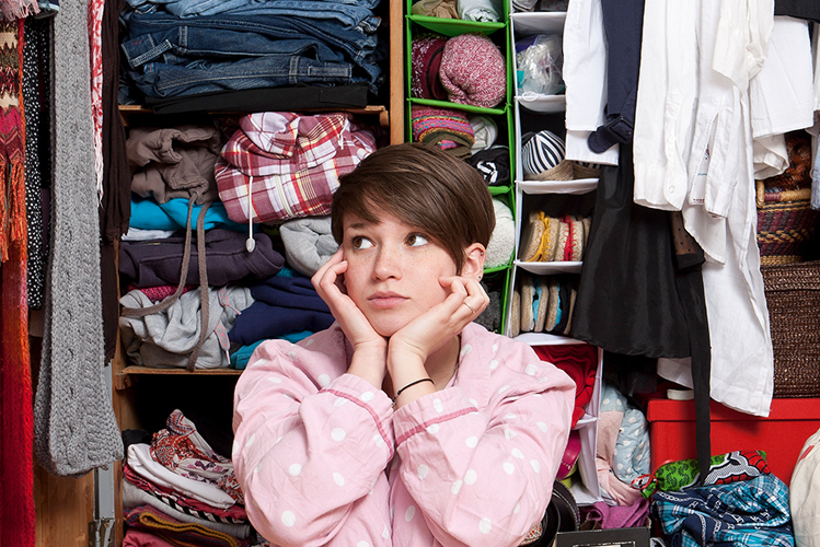 Das Foto zeigt eine junge Frau, die vor ihrem Kleiderschrank sitzt.