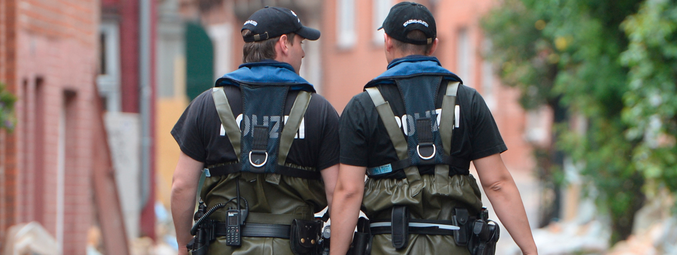 Zwei Polizisten laufen durch das Hochwasser in einer Stadt mit Schutzkleidung