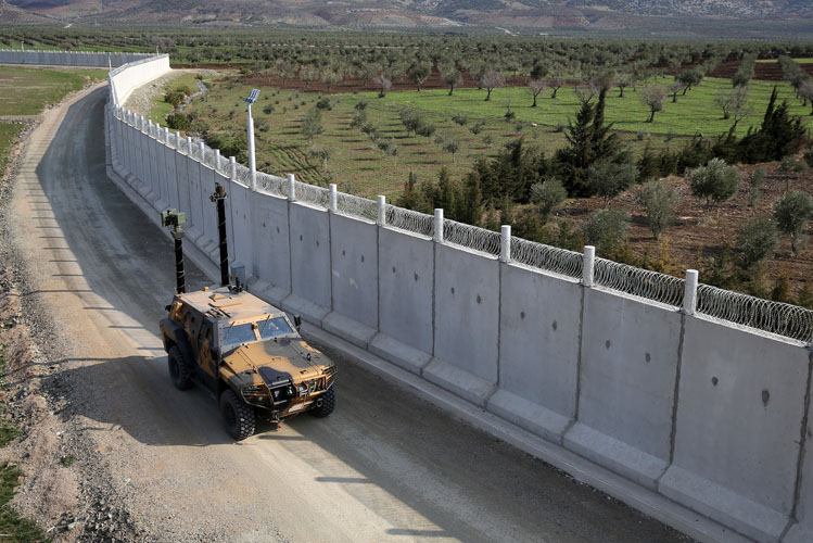 Ein Geländewagen fährt an einer sehr langen Mauer, die eine Grenze ist, entlang