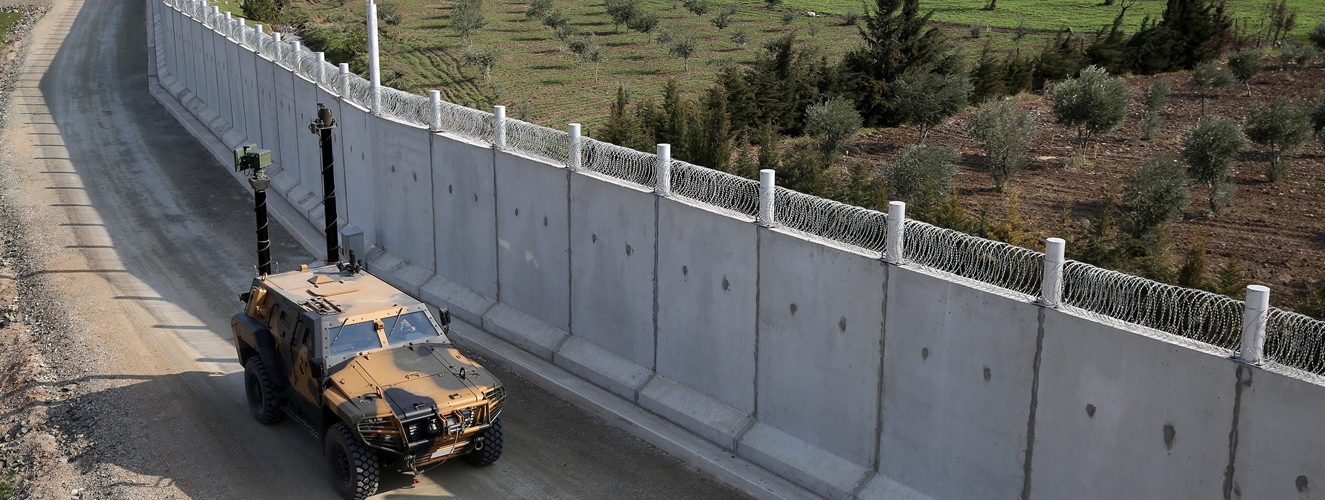 Ein Geländewagen fährt an einer sehr langen Mauer, die eine Grenze ist, entlang