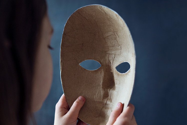 Eine psychopathische Frau hält eine Maske vor sich, im Begriff sich diese aufzusetzen