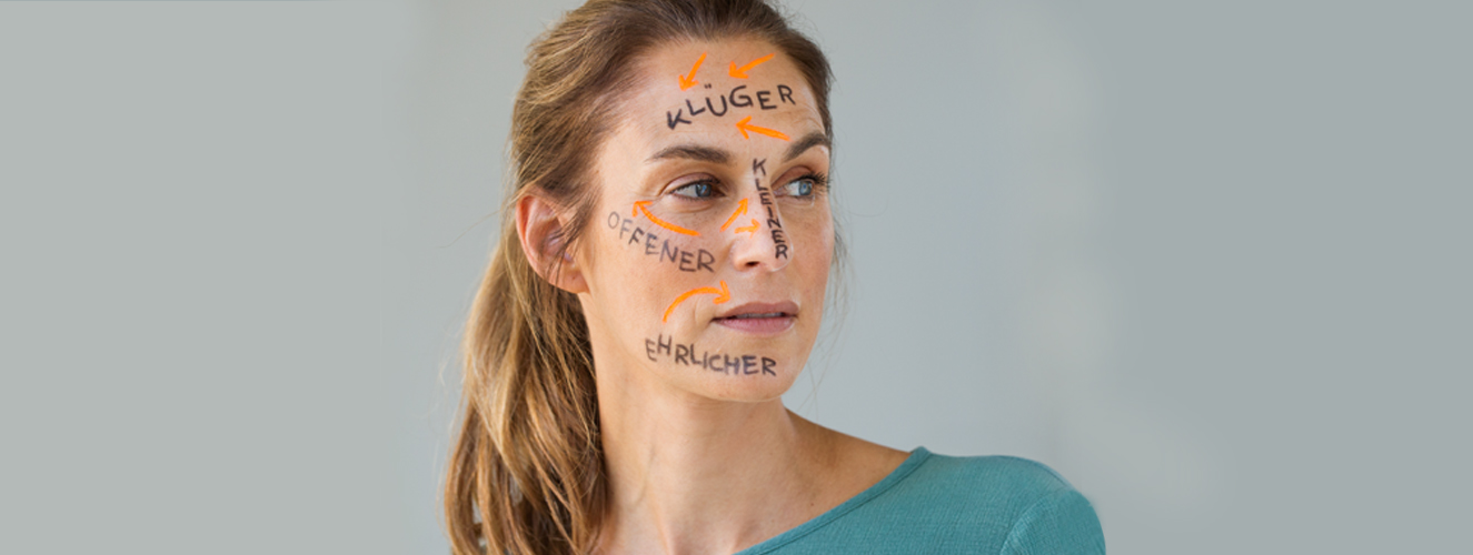 Ein Frau mit gemalten Wörtern auf dem Gesicht, wie zum Beispiel "Klüger", "Offener" und "Ehrlicher" schaut voller Zweifel in die Ferne