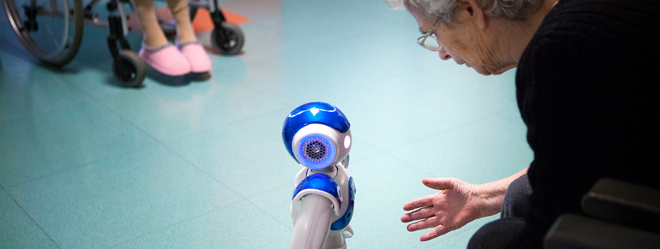 Foto zeigt eine alte Frau im Pflegeheim, die sich zu einem Roboter herunterbeugt 