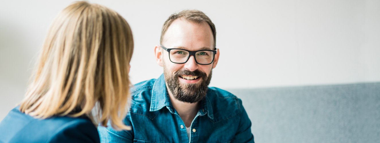 Foto zeigt einen Mann, der sich klug und zurückhaltend mit einer Frau unterhält.