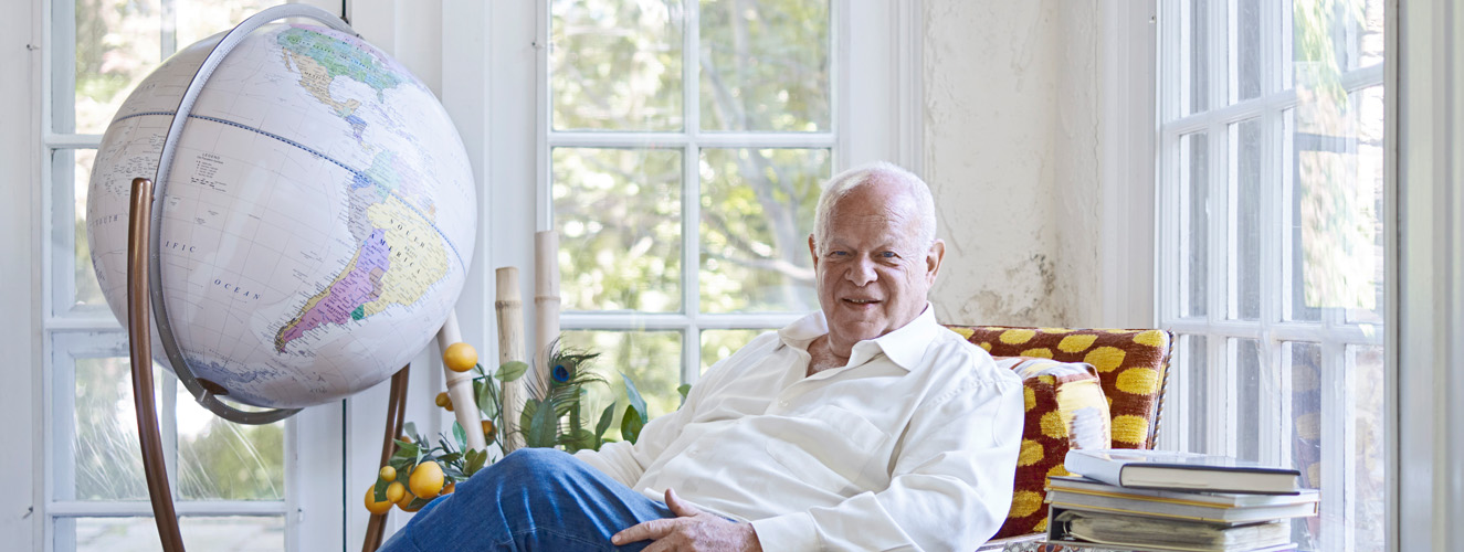 Der Autor, Martin Seligman, sitzt lächelnd in einem roten Sessel mit gelben Punkten, neben sich einen Globus