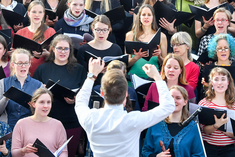 Ein Dirigent steht vor einem Chor, der glücklich singt