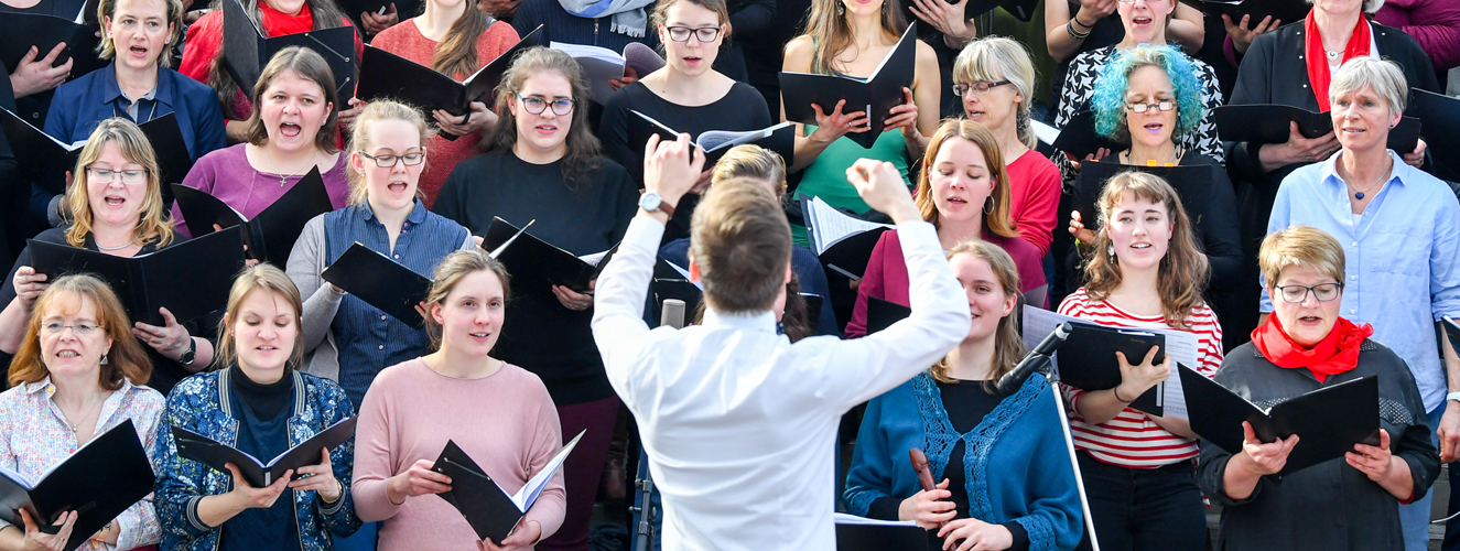 Ein Dirigent steht vor einem Chor, der glücklich singt