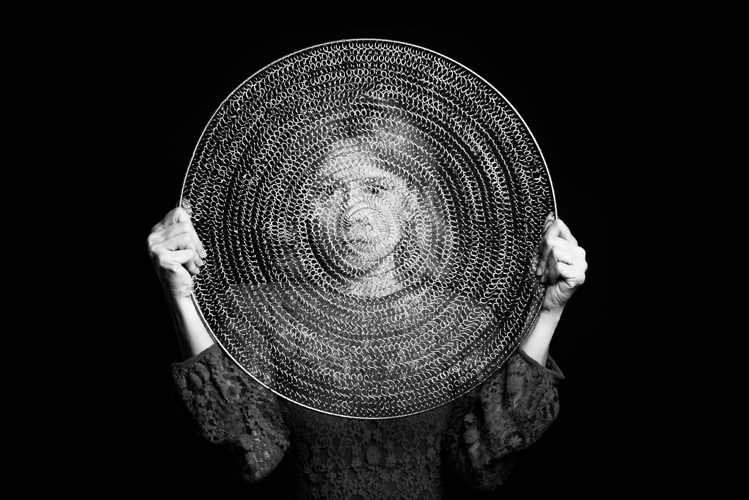 Foto zeigt eine Frau, die einen Kreis aus Metallgeflecht vor ihr Gesicht hält, um sich vor negativen Gefühlen zu schützen