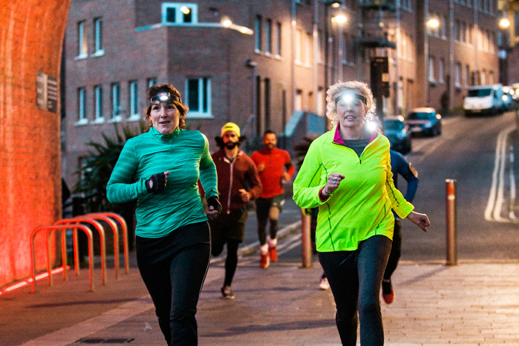 Menschen joggen in der Dämmerung mit Stirnlampe auf dem Kopf und fügen sich damit dem Zeitalter der Fitness
