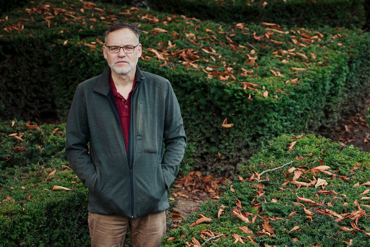 Stefan Lange, der in seinem YouTube-Kanal schonungslos über seine Suizidversuche spricht, steht allein vor einer Hecke mit Herbstlaub