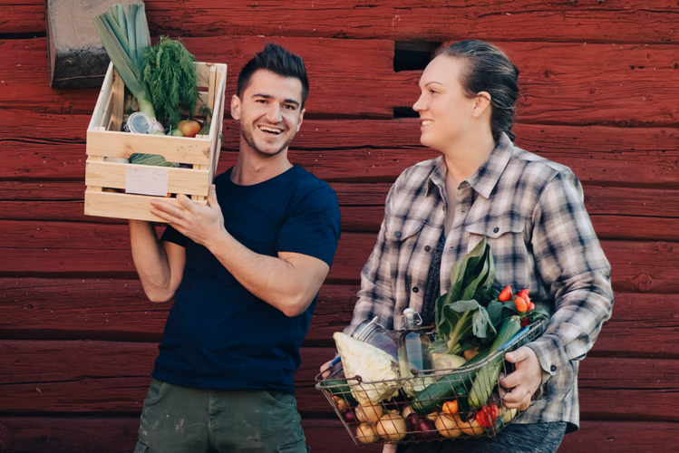 Junge Biobauern halten lachend und selbstgerecht ihre Gemüsekörbe und denken sie sind besser als andere