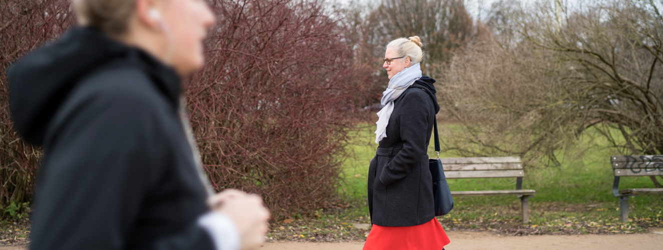 Die Autorin Isabel Bogdan läuft mit rotem Rock, dunklem Mantel und Schal im Park spazieren