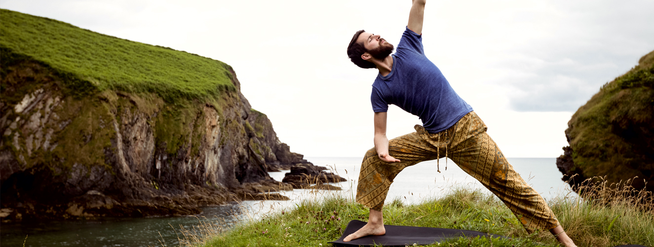 Foto zeigt einen Mann, der am Meer Yoga übt.