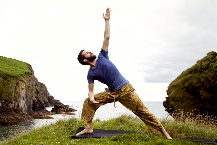 Foto zeigt einen Mann, der am Meer Yoga übt.