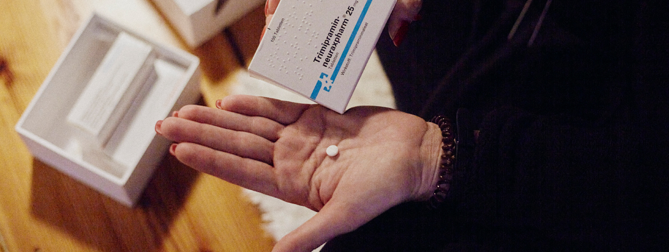 Eine Frau hält in der linken Hand eine weiße Tablette und in der rechten Hand die Verpackung