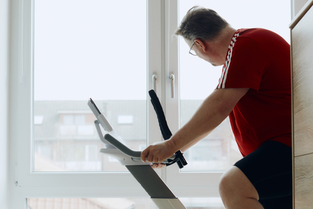 Ein übergewichtiger Mann sitzt auf einem Fitnessgerät und schaut dabei aus dem Fenster