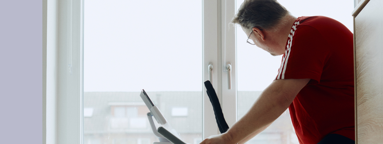 Ein übergewichtiger Mann sitzt auf einem Fitnessgerät und schaut dabei aus dem Fenster