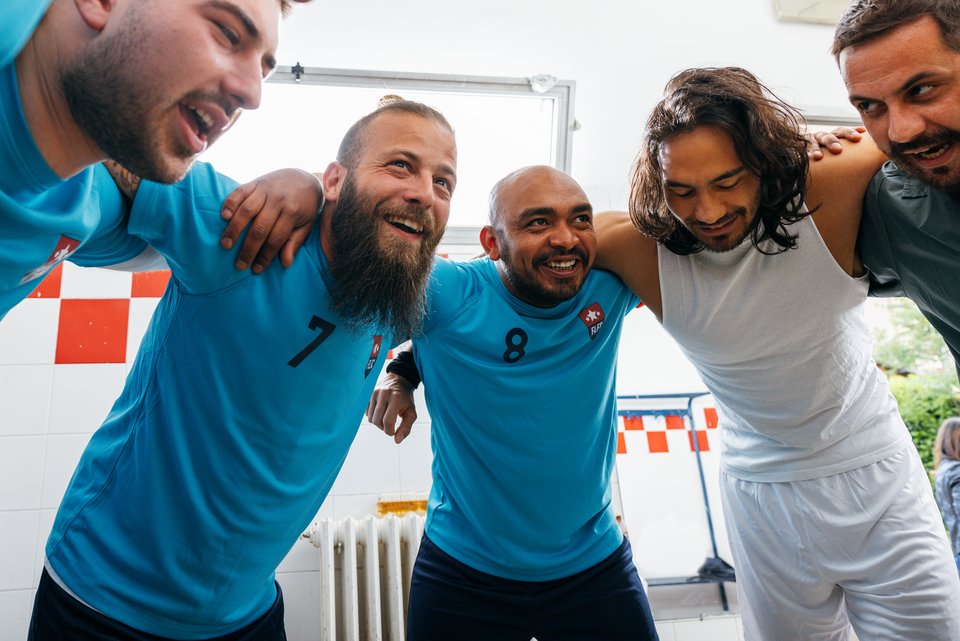 Ein Mann spielt in seiner Freizeit in einem Fußballverein und steht im Kreis mit seinen Freunden in der Kabine