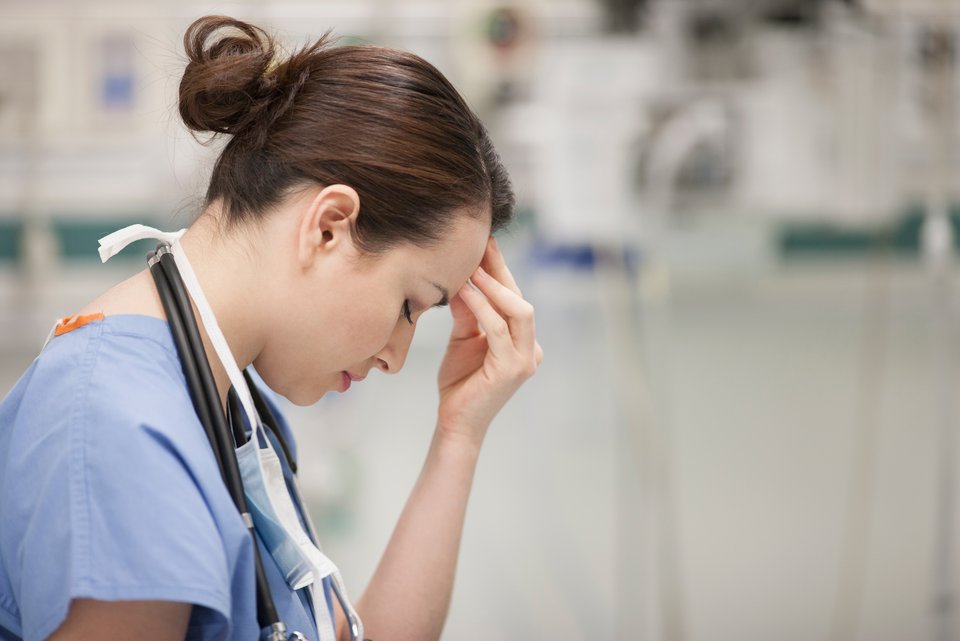Eine Pflegekraft in einem Krankenhaus hält sich gestresst die Stirn und hat dabei den Kopf gesenkt