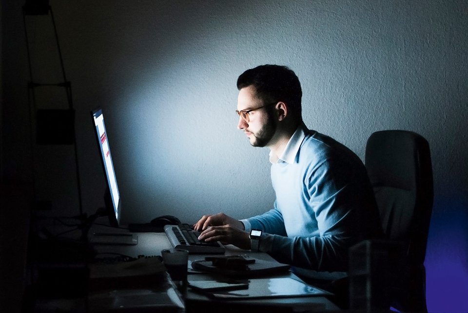 Foto zeigt einen Mann, der nachts am Computer arbeitet.