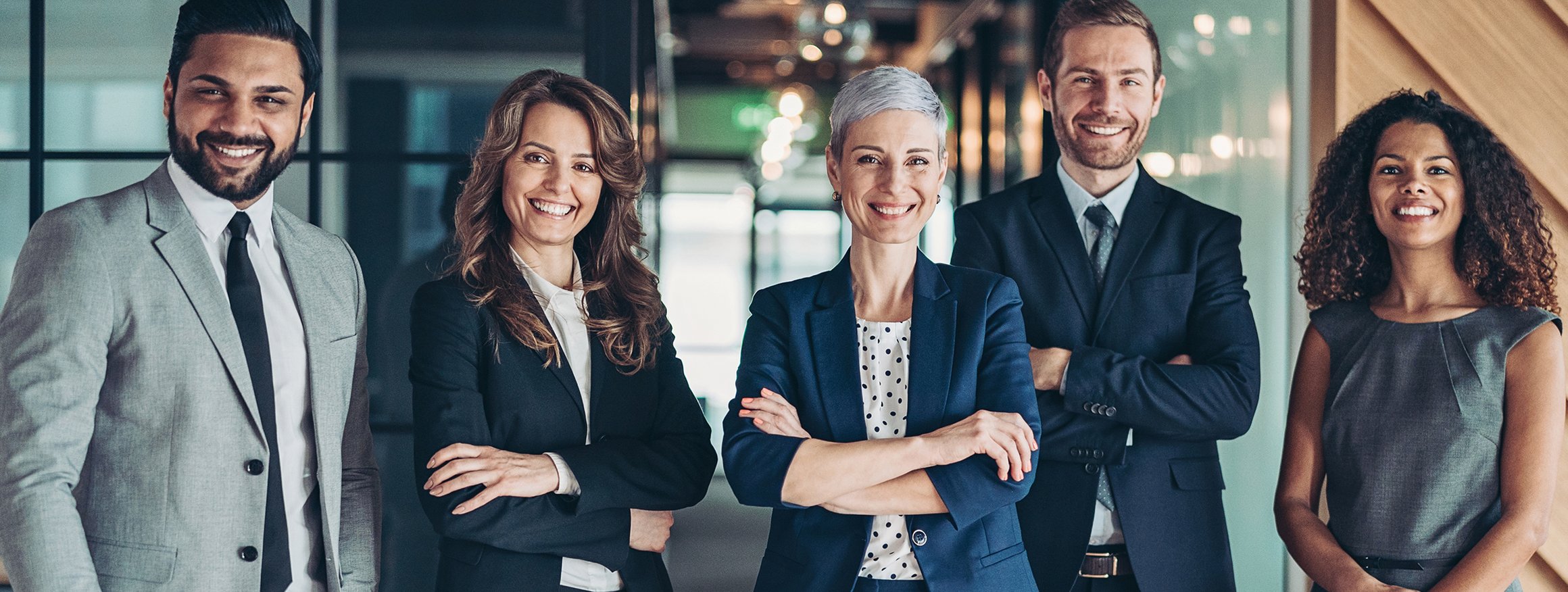 Diverses Team steht in Business-Kleidung in einer Reihe und lächelt gutgelaunt