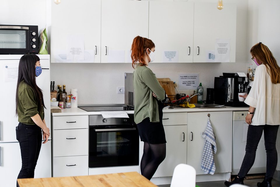 Eine Frau steht in der Büroküche und bedient den Kaffeeautomaten, während hinter ihr zwei Kolleginnen warten, bis sie dran sind