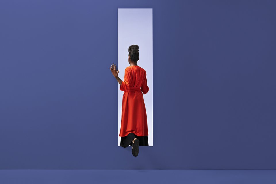 Frau in rotem Kleid geht durch einen Eingang an einer großen blauen Wand