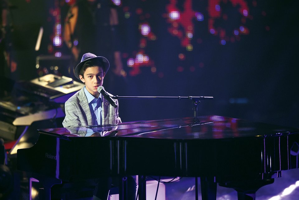Ein Junge sitzt mit Anzug und Hut in einer Casting-Show am Klavier und singt in ein Mikro