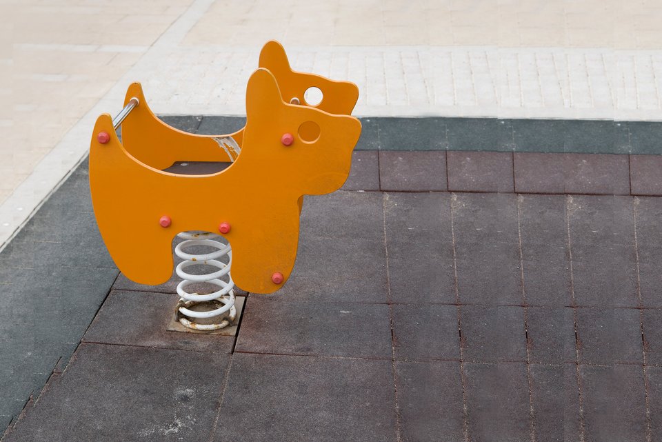 Ein orangefarbenes Wippgerät in Tierform steht auf einem Kinderspielplatz und der Boden ist betoniert