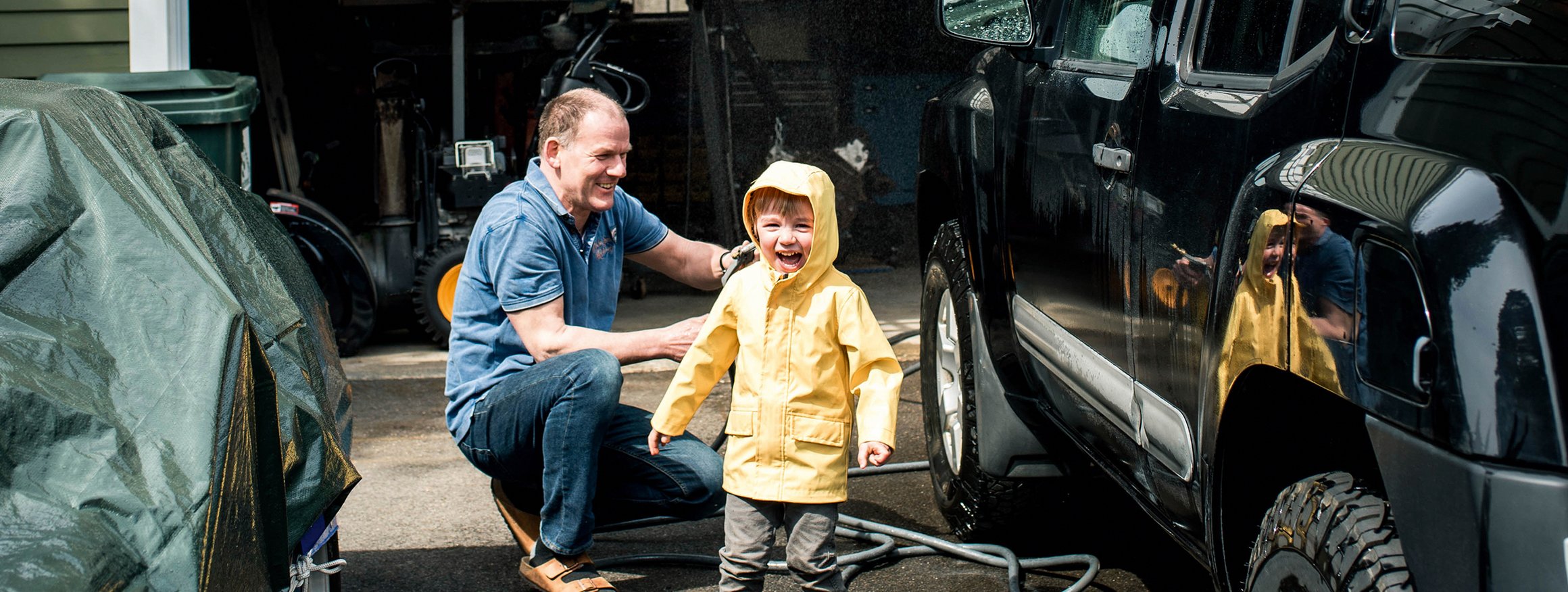Ein Mann wäscht fröhlich gemeinsam mit einem kleinen Jungen seinen schwarzen SUV