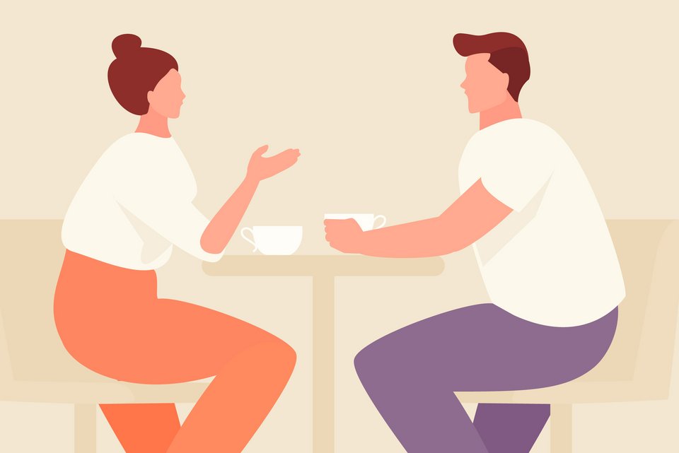 Eine Frau und ein Mann sitzen an einem Tisch und er hört ihr verständnisvoll zu, während sie redet