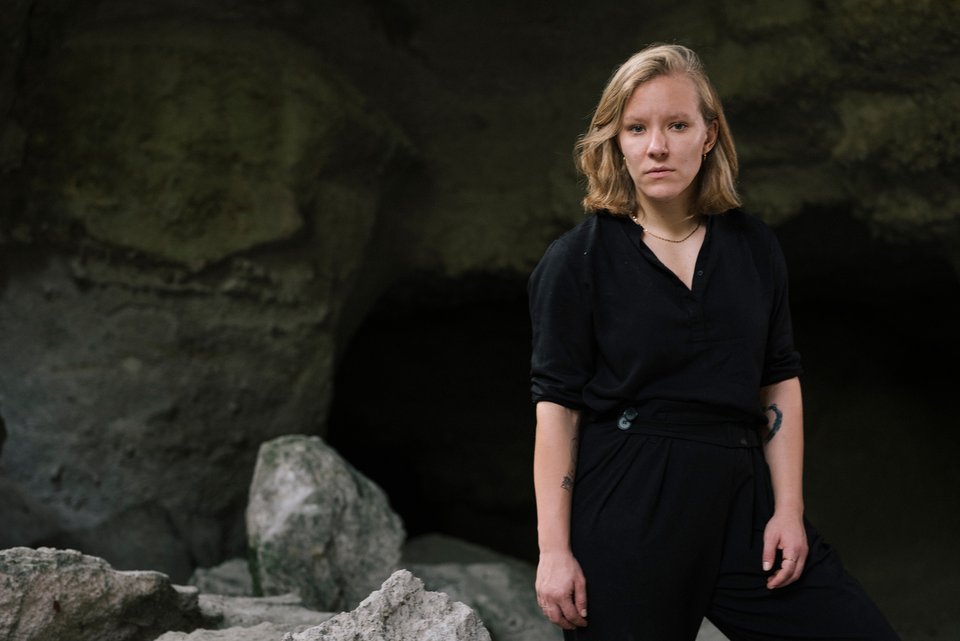 Die Autorin Raphaela Edelbauer steht zwischen Felsen vor einem Höhleneingang