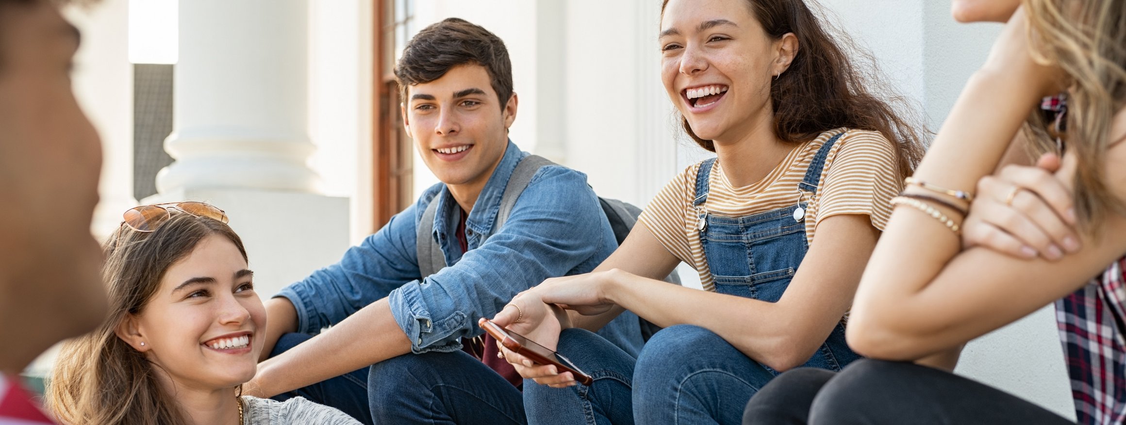 Eine Gruppe von pubertierenden Teenagern sitzen lachend auf einer Treppenstufe vor einem Gebäude